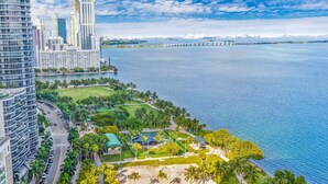 A high-rise building with a curved facade, a waterfront park with palm trees, and a bridge in the background. - Bayfront Long-Stay | Premium Amenities | StayCozy (Miami)