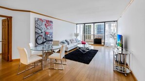 A modern living room with a glass dining table, white sofas, and a large window with a city view. - Bayfront Long-Stay | Premium Amenities | StayCozy (Miami)