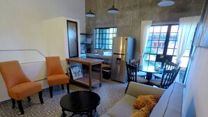Ein kompakter Wohnbereich mit einer Couch, zwei orangefarbenen Sesseln, einem kleinen Tisch, einem schwarzen Couchtisch, einem Kühlschrank und einem Essbereich mit Stühlen und Tisch.