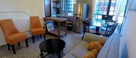 A compact living space with a sofa, two orange chairs, a small table, a black coffee table, a refrigerator, and a dining area with chairs and a table.