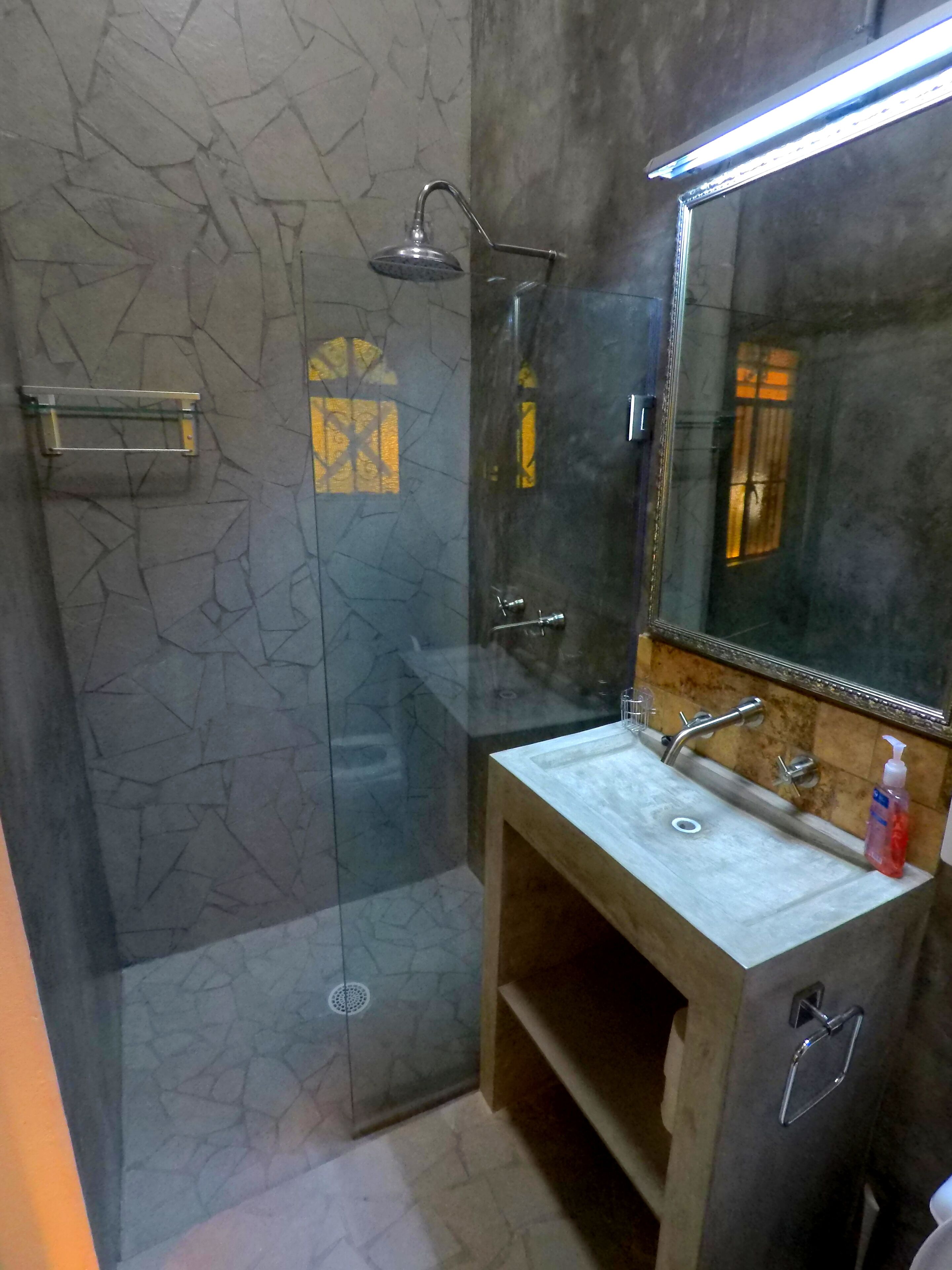 Een badkamer met een douchecabine van glas, een wastafel met spiegel erboven en een zeepdispenser op de wastafel.
