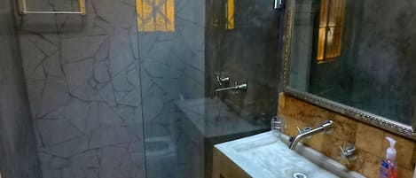 Een badkamer met een douchecabine van glas, een wastafel met spiegel erboven en een zeepdispenser op de wastafel.