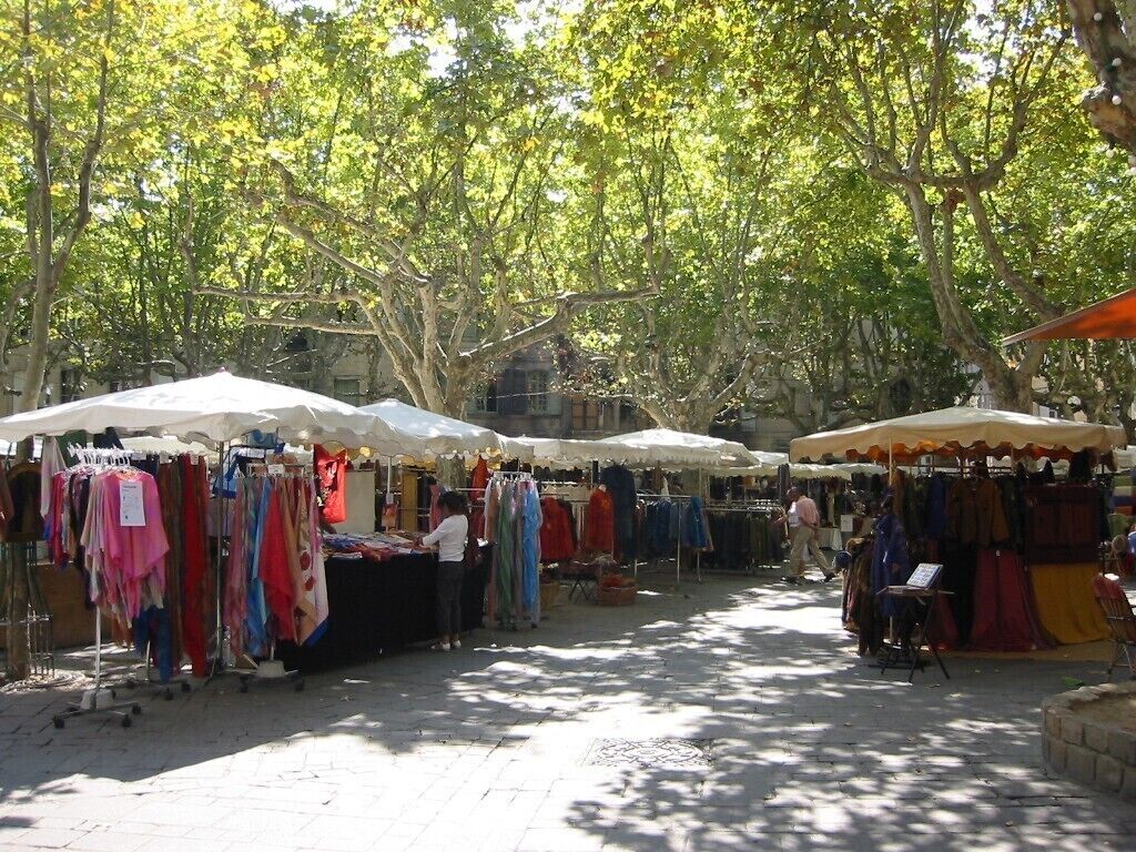 Un marché en plein air où les étals sont couverts de toiles blanches et oranges, et où sont vendus divers articles de textile.