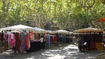 Un marché en plein air où les étals sont couverts de toiles blanches et oranges, et où sont vendus divers articles de textile.