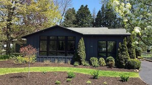 Ein modernes, zweistöckiges Haus mit dunkler Fassade, großen Fenstern und einem gepflegten Garten mit verschiedenen Sträuchern und einer Rasenfläche.