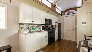 Une cuisine de taille réduite avec des meubles blancs, un réfrigérateur noir, un four à micro-ondes et une cuisinière.