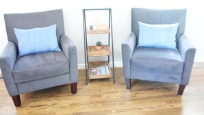 Deux fauteuils gris avec des coussins bleus et une petite table d’appoint en bois, sur laquelle se trouvent une petite plante et des livres.