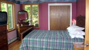 Un dormitorio con cama, cómoda y ventana con vista a árboles.