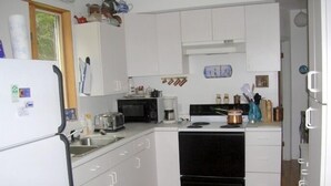 Cocina compacta con armarios blancos, estufa negra, microondas y lavabo.