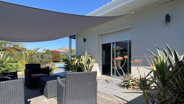 Een overdekt terras met buitenmeubilair, een zwembad en een huis met een schuifdeur.