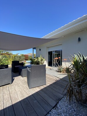 A covered patio with outdoor furniture, a pool, and a house with a sliding glass door.