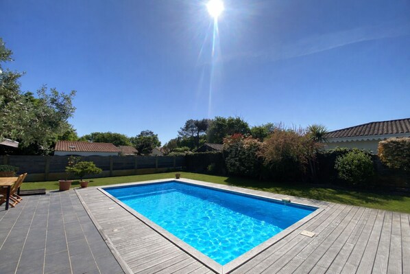 A rectangular swimming pool with a wooden deck surrounding it, a clear blue sky, and a sunny day.
