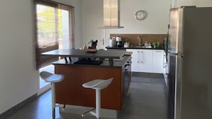 Een moderne keuken met een centraal eiland, barkrukken, een koelkast en een klok aan de muur.