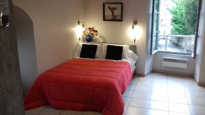 A bedroom with a red bedspread, two black pillows, a vase with flowers, and a painting on the wall.