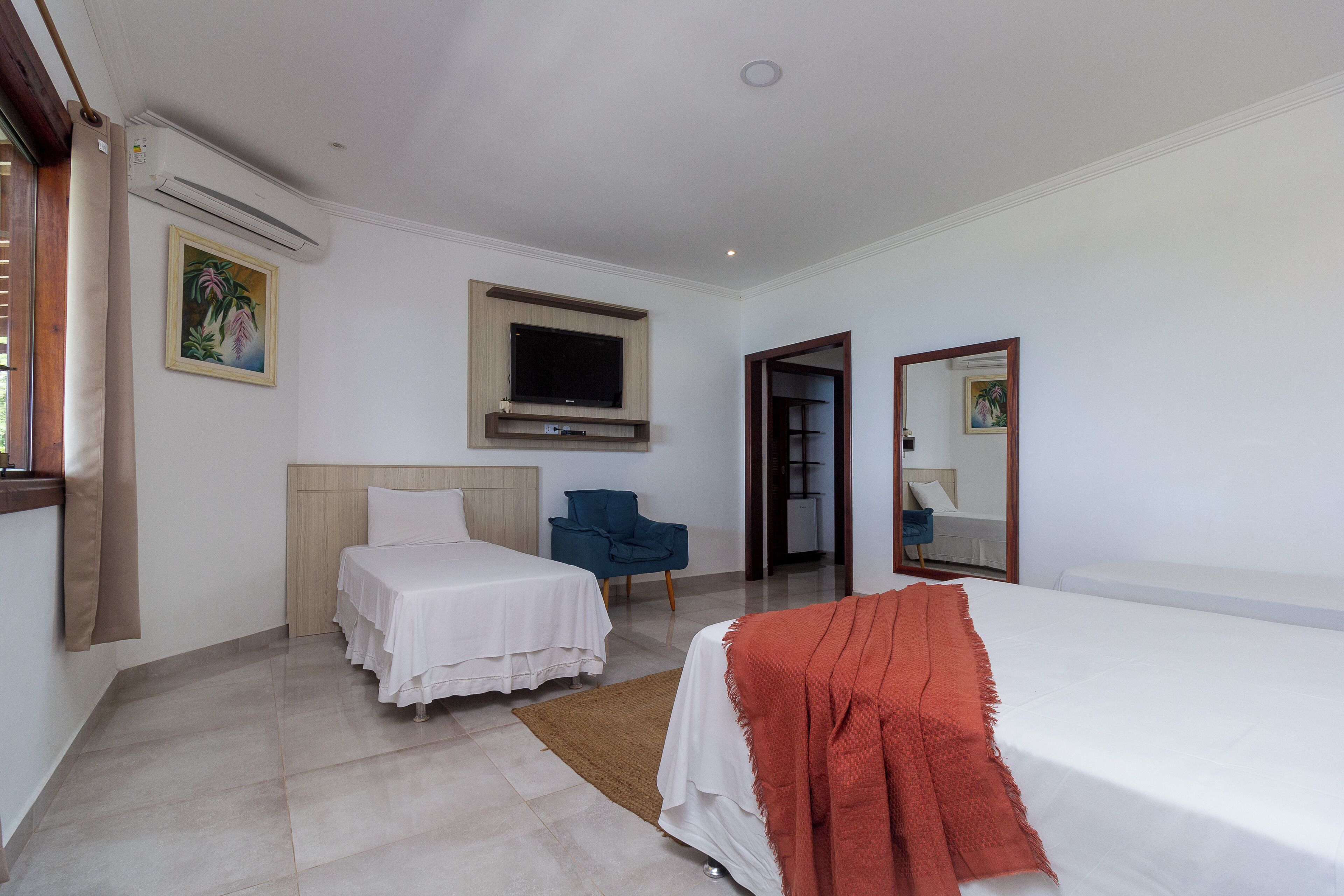 A hotel room with two beds, a TV, a chair, and a mirror.