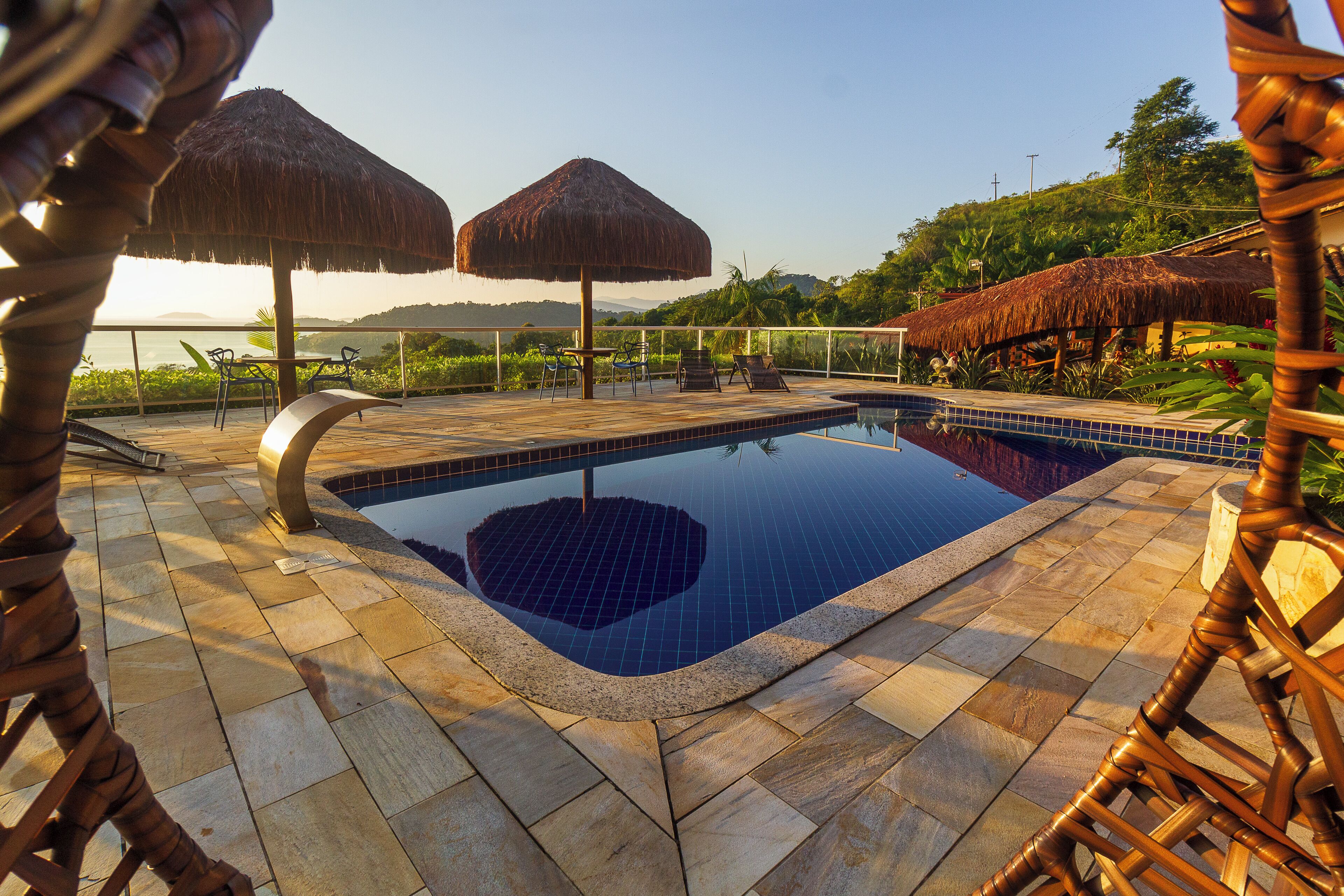 Ein Poolbereich mit gefliestem Deck, Liegestühlen und Strohdächern.