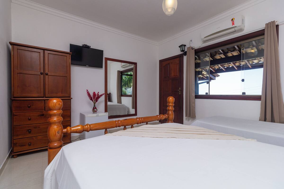 Une chambre à coucher avec un lit en bois, une commode, un téléviseur fixé au mur et une fenêtre avec des rideaux.