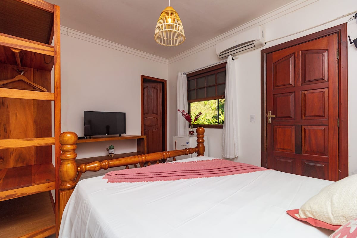 Une chambre à coucher avec un lit en bois, une télévision, une armoire et une fenêtre avec des rideaux.