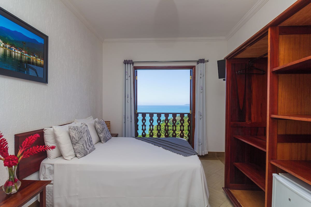 Une chambre à coucher avec un lit, une armoire en bois, une table de chevet, un vase avec des fleurs et un tableau au mur.