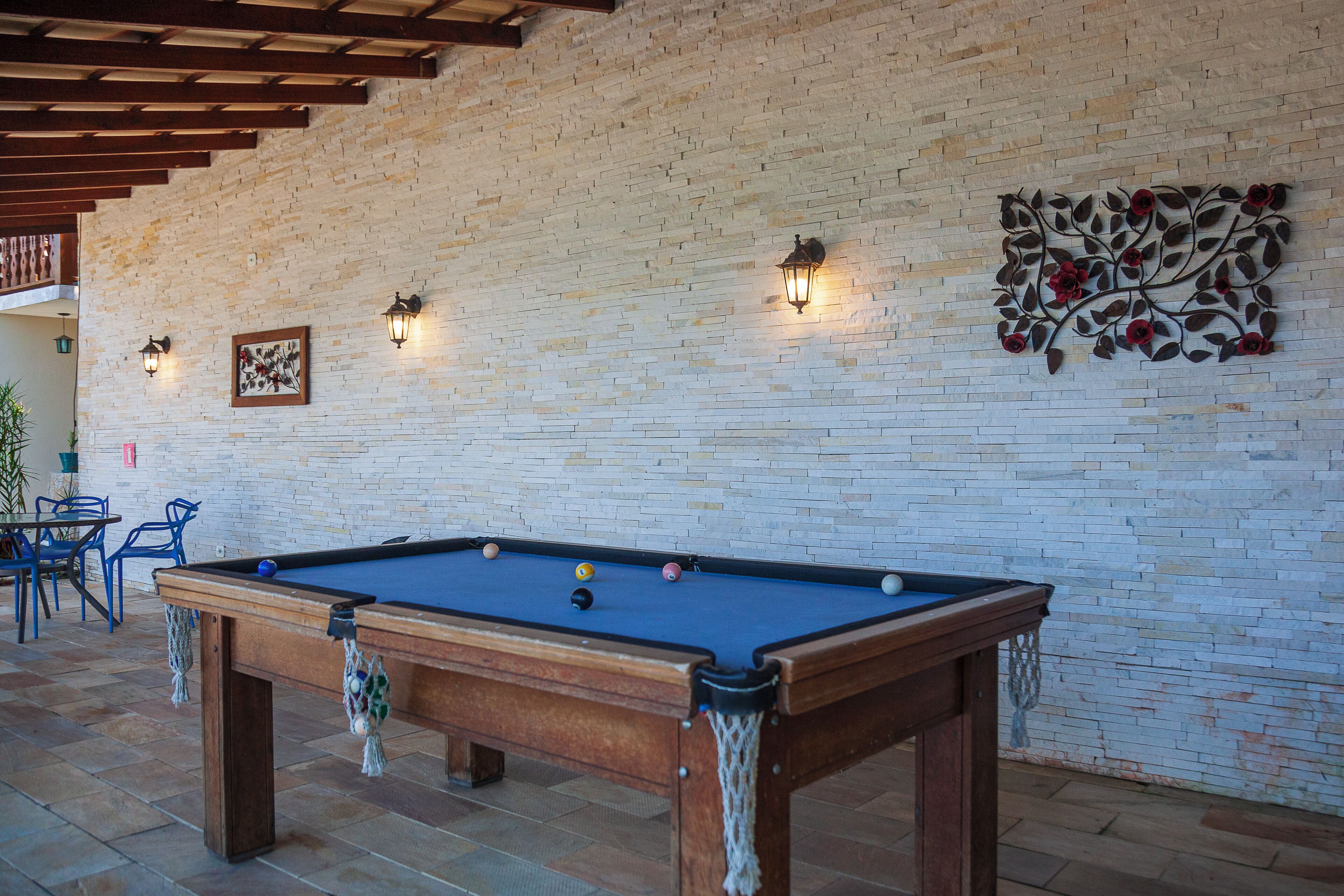 Una mesa de billar en una sala con pared de ladrillo, vigas de techo de madera y luces fijadas a la pared.