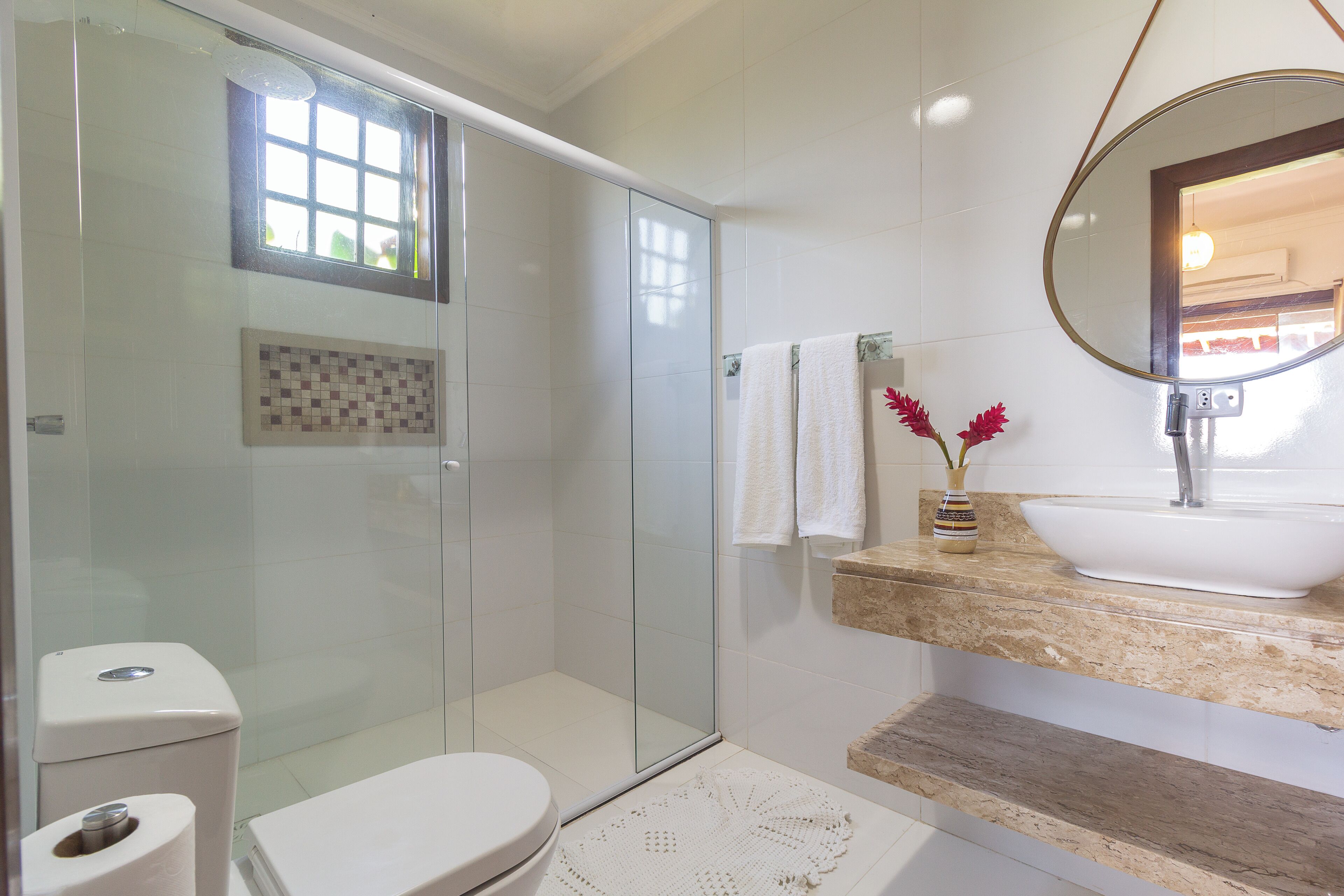 A modern bathroom with a glass-enclosed shower, a white toilet, a sink with a marble countertop, and a mirror.
