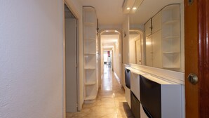 Ein schmaler Flur mit einer weißen Tür rechts, einer weißen Wand und einem weißen Schrank mit Regalen links.