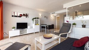 Ein modernes Wohnzimmer mit Flachbildfernseher, Essbereich und einer Sitzecke mit Sofa und Sesseln.