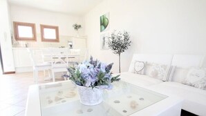 Uma sala de estar moderna com uma mesa de centro de vidro, sofá branco e um espaço de refeições com cadeiras e mesa.