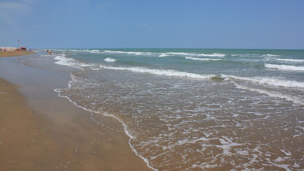 Uma praia com céu claro e ondas suaves.