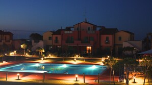 Piscina cercada por área bem iluminada com um edifício grande ao fundo.
