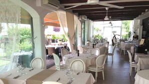 Um restaurante com toalhas de mesa brancas, cadeiras brancas e vista para o jardim.