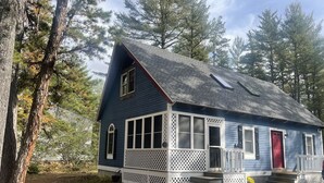 Een blauw huis met een rode deur, een witte veranda en een kleine voortuin.