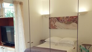 Ein Schlafzimmer mit einem Bett, einem Deckenventilator, einem Fernseher auf einem Standfuß und einem Bild an der Wand.