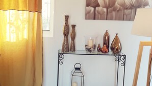 Ein Zimmer mit Fenster, Vorhang, einem Wandbild, einem Konsolentisch mit Dekoration und einer Stehlampe.