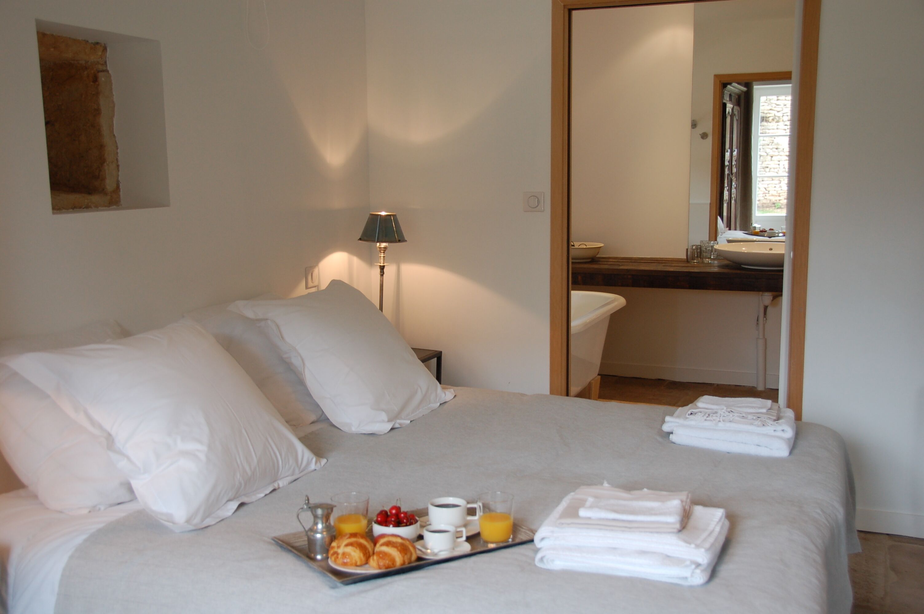 Una camera d'albergo con un letto, un vassoio per la colazione, una lampada e un bagno visibile attraverso uno specchio.