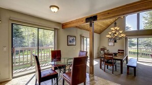 A spacious dining area with a high ceiling and large windows, offering views of a wooded area.