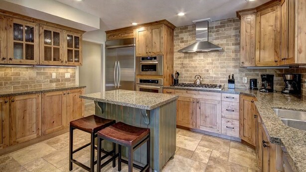 A kitchen with wooden cabinets, a granite countertop, stainless steel appliances, and a central island with stools.