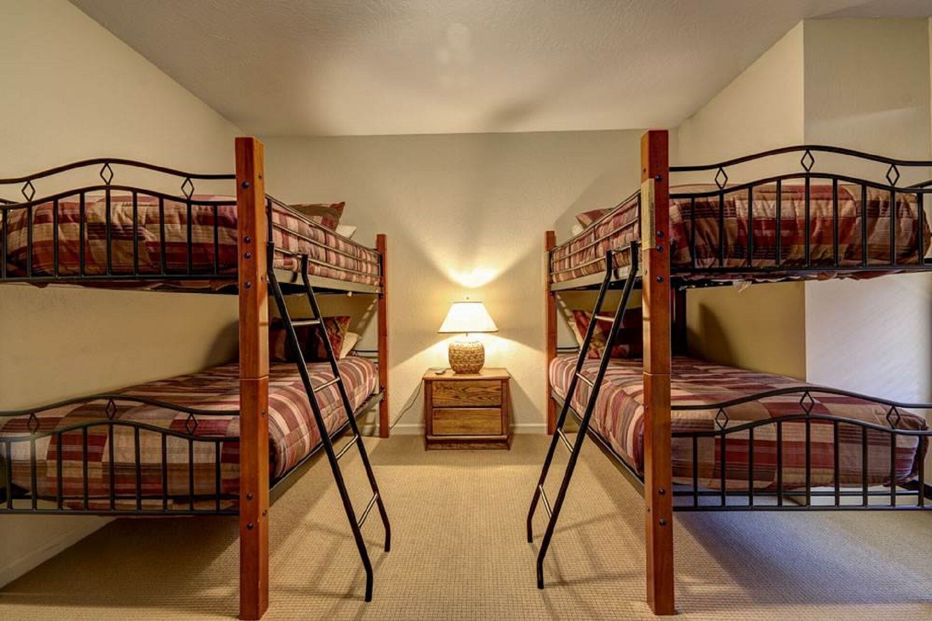 Una habitación con dos literas, una mesita de noche pequeña con lámpara y suelo alfombrado.