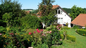 A white house with a red roof surrounded by lush greenery and flowering plants. - Lovingly furnished new FEWO for 2 people in an absolutely quiet location (Horn-Bad Meinberg / Feldrom)