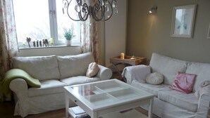 A living room with two white sofas, a glass coffee table, and a small side table with a candle. - Lovingly furnished new FEWO for 2 people in an absolutely quiet location (Horn-Bad Meinberg / Feldrom)