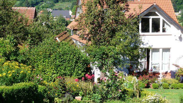 A white house with a red-tiled roof, surrounded by lush greenery and flowering plants. - Lovingly furnished new FEWO for 2 people in an absolutely quiet location (Horn-Bad Meinberg / Feldrom)
