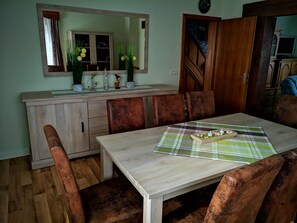 Ein Essbereich mit einem Holztisch, sechs Stühlen, einem Spiegel über dem Tisch und einem Schrank mit Spüle.