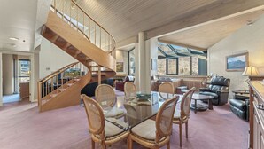Un vaste espace de vie agrémenté d’un escalier en bois, d’une table à manger en verre entourée de chaises en osier et d’un canapé en cuir.