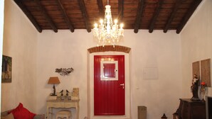 Habitació amb una porta vermella, un xandall, una paret blanca, un sostre de fusta, una taula petita amb una làmpada i un sofà amb un coixí vermell.