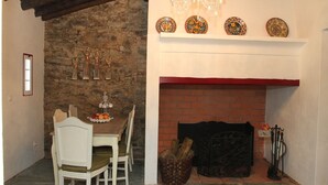 Una zona de menjador amb una paret de pedra, una llar de foc amb mantell vermell i un candelabrum.