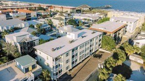 A coastal residential area with multi-story buildings, a pier extending into the sea, and a clear view of the ocean.