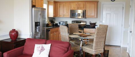 A compact living space with a kitchenette, a red sofa, wicker chairs, and a dining table.