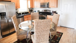 A kitchen with wooden cabinets, stainless steel appliances, a glass dining table, and woven chairs.