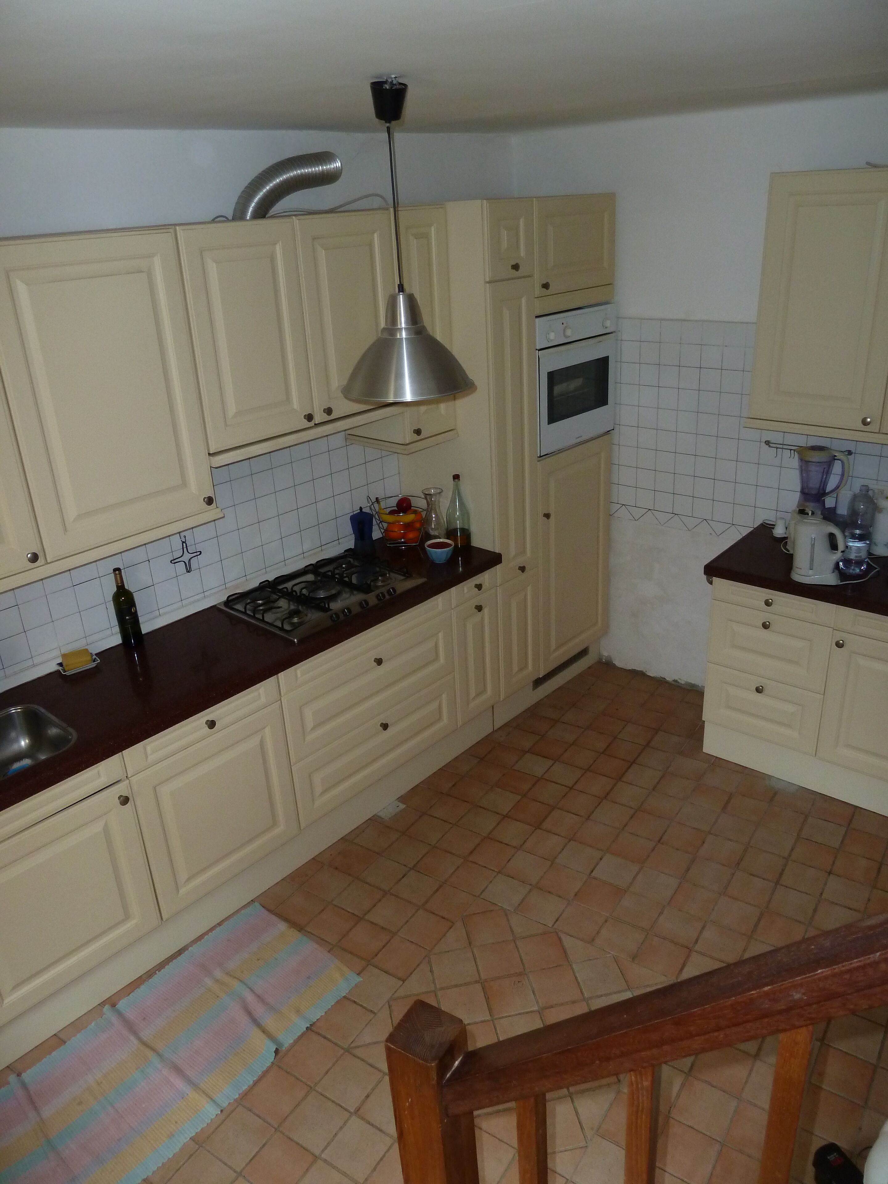Une cuisine avec des meubles blancs, une cuisinière à gaz, un four à micro-ondes et un mixeur sur le plan de travail.