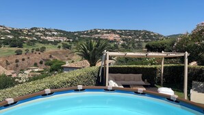 A swimming pool with a pergola and outdoor seating area, surrounded by lush greenery and a view of a hillside residential area. - Air-conditioned villa, 4-star rating, Ste-Maxime residential area, golf view (Sainte-Maxime)